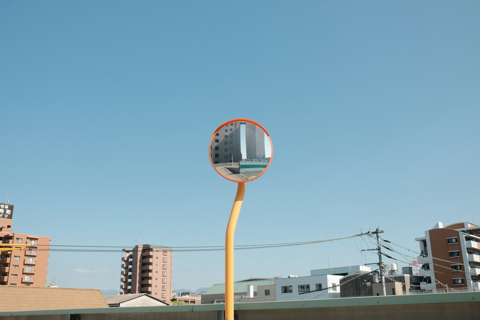A convex mirror reflects buildings under a blue sky.