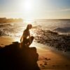 Woman crouching on a rocky beach at sunset