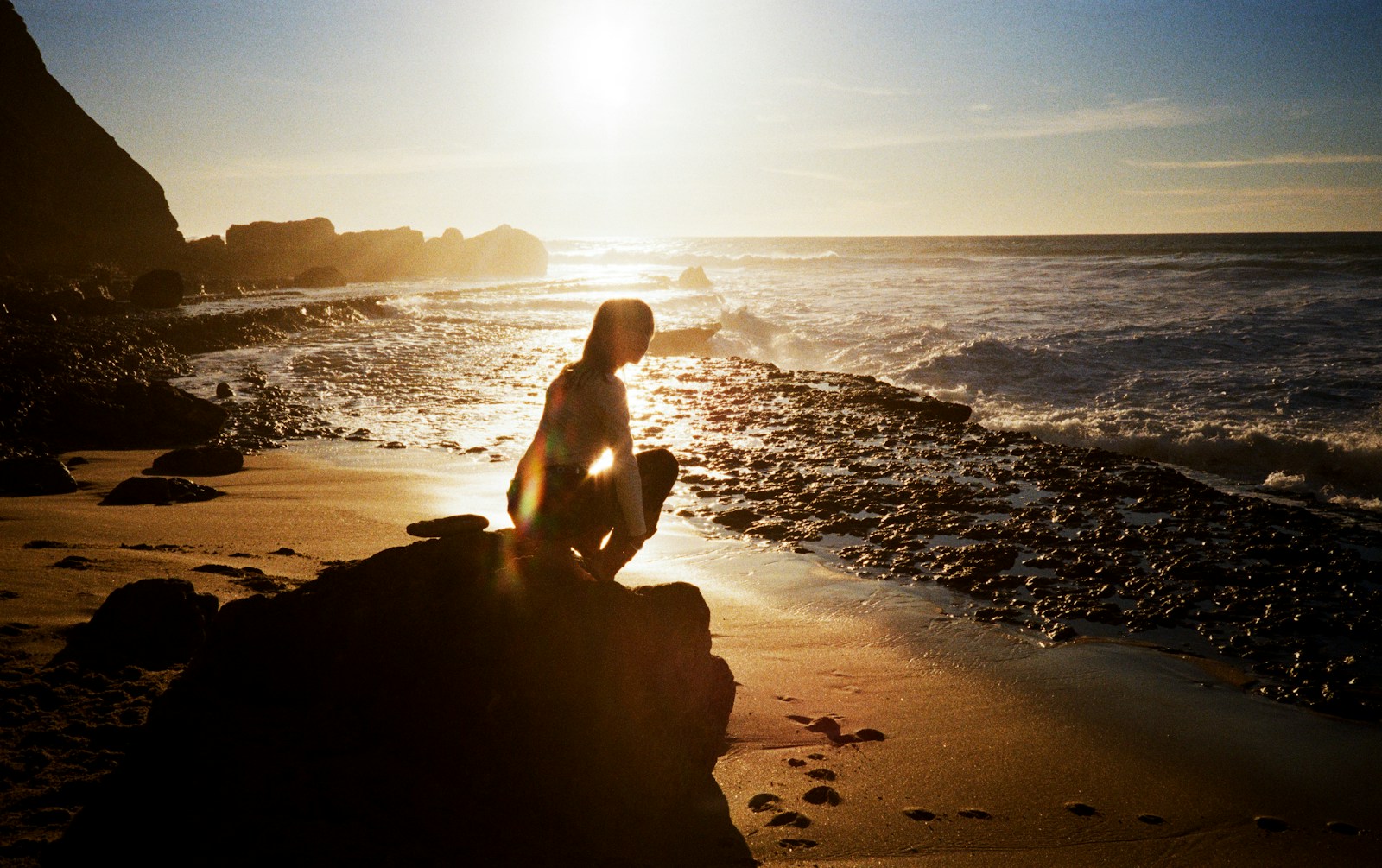 Woman crouching on a rocky beach at sunset
