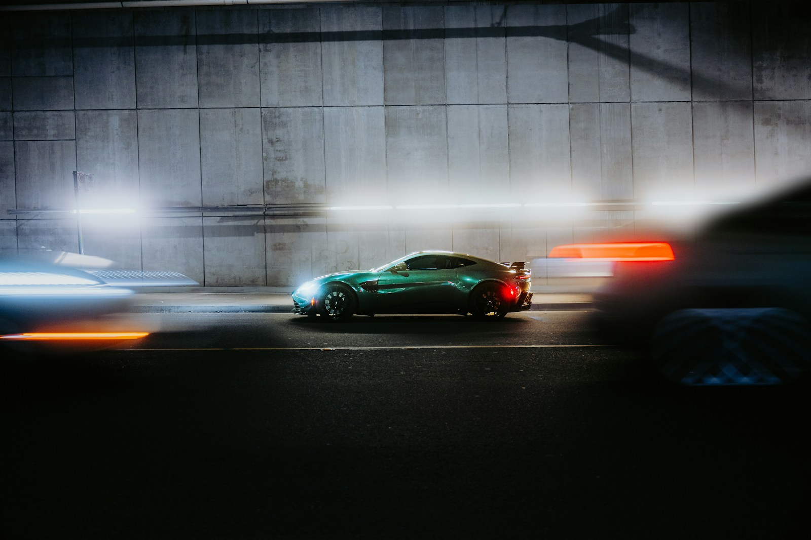 A green car drives through a dark tunnel.