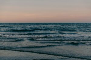 Gentle ocean waves wash ashore under a pastel sky.