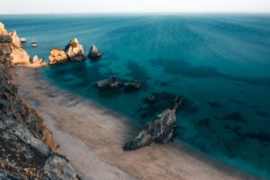Sandy beach, clear blue ocean, and rock formations from above.
