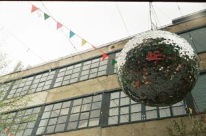 Large disco ball and colorful flags outside an industrial building.