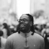 A smiling man with glasses and dreadlocks in a crowd.