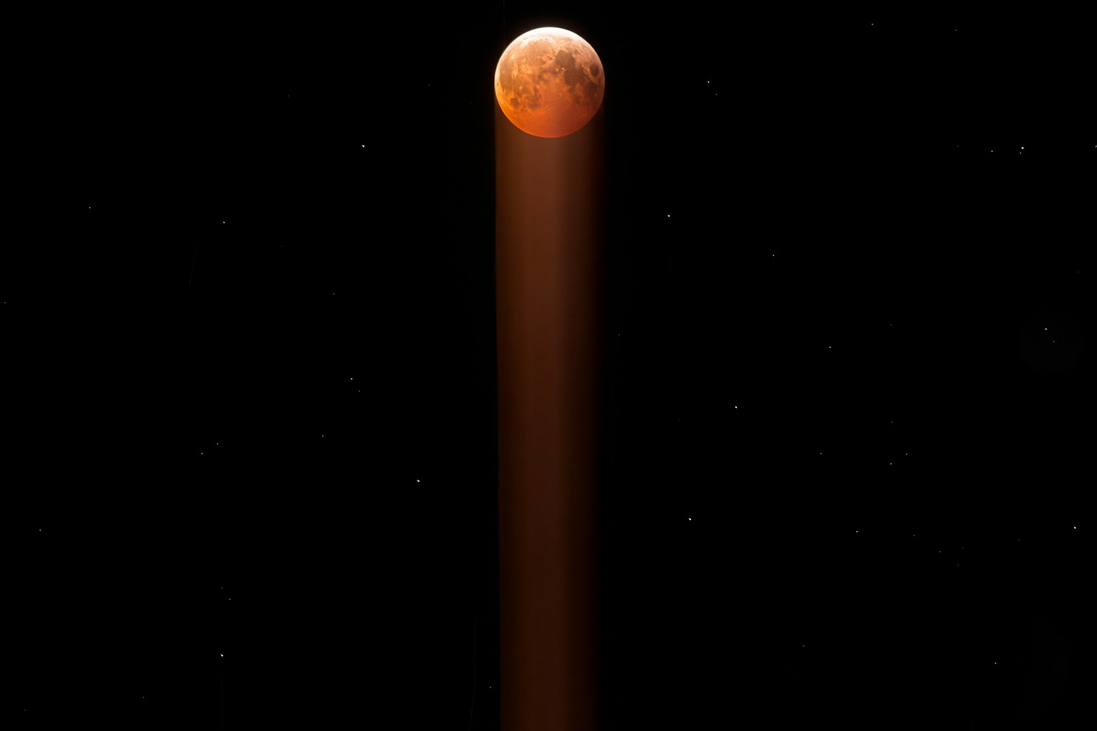 Blood moon in starry night sky with light beam