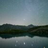 Starry night sky over a calm mountain lake