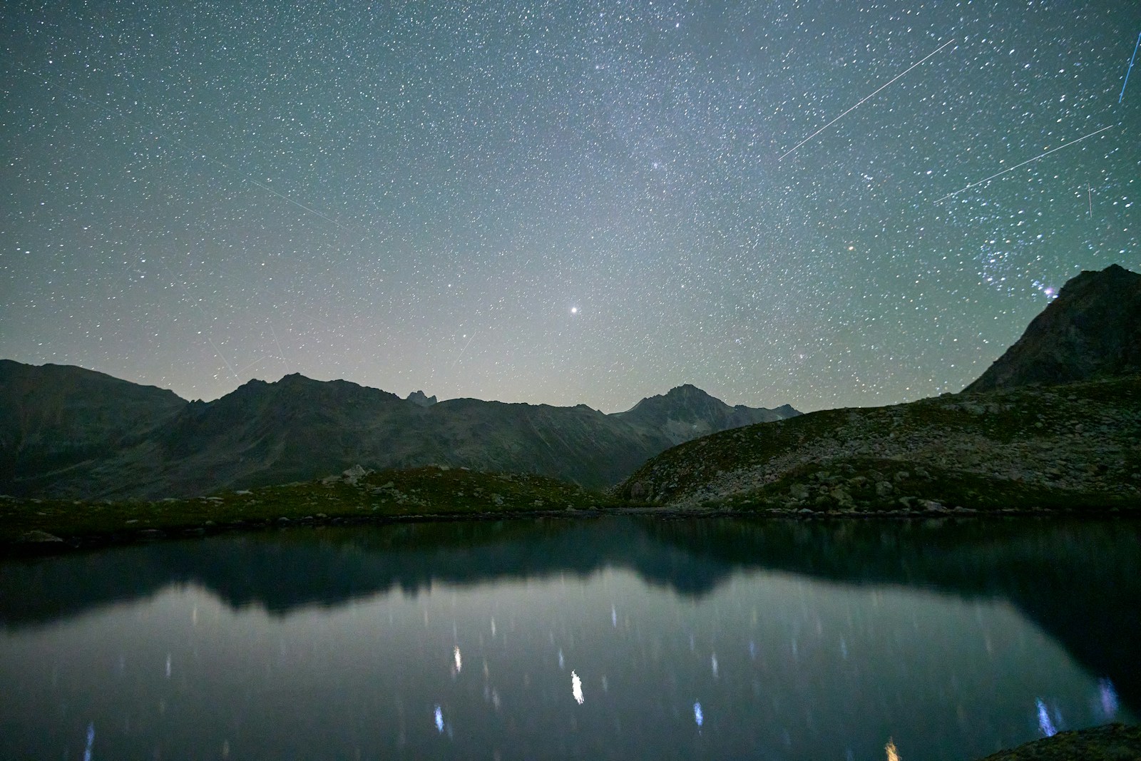 Starry night sky over a calm mountain lake
