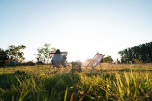 Person relaxing in a chair in a sunny, grassy field.