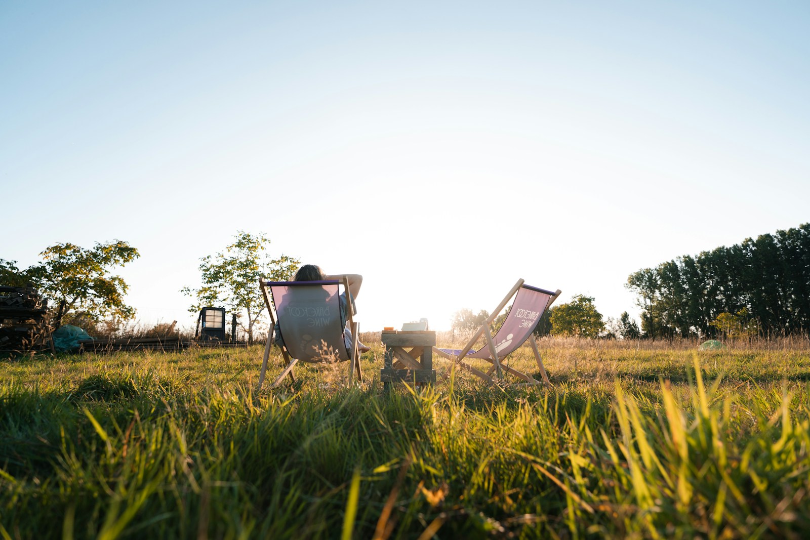Person relaxing in a chair in a sunny, grassy field.