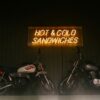 Neon sign advertises hot and cold sandwiches, with motorcycles.