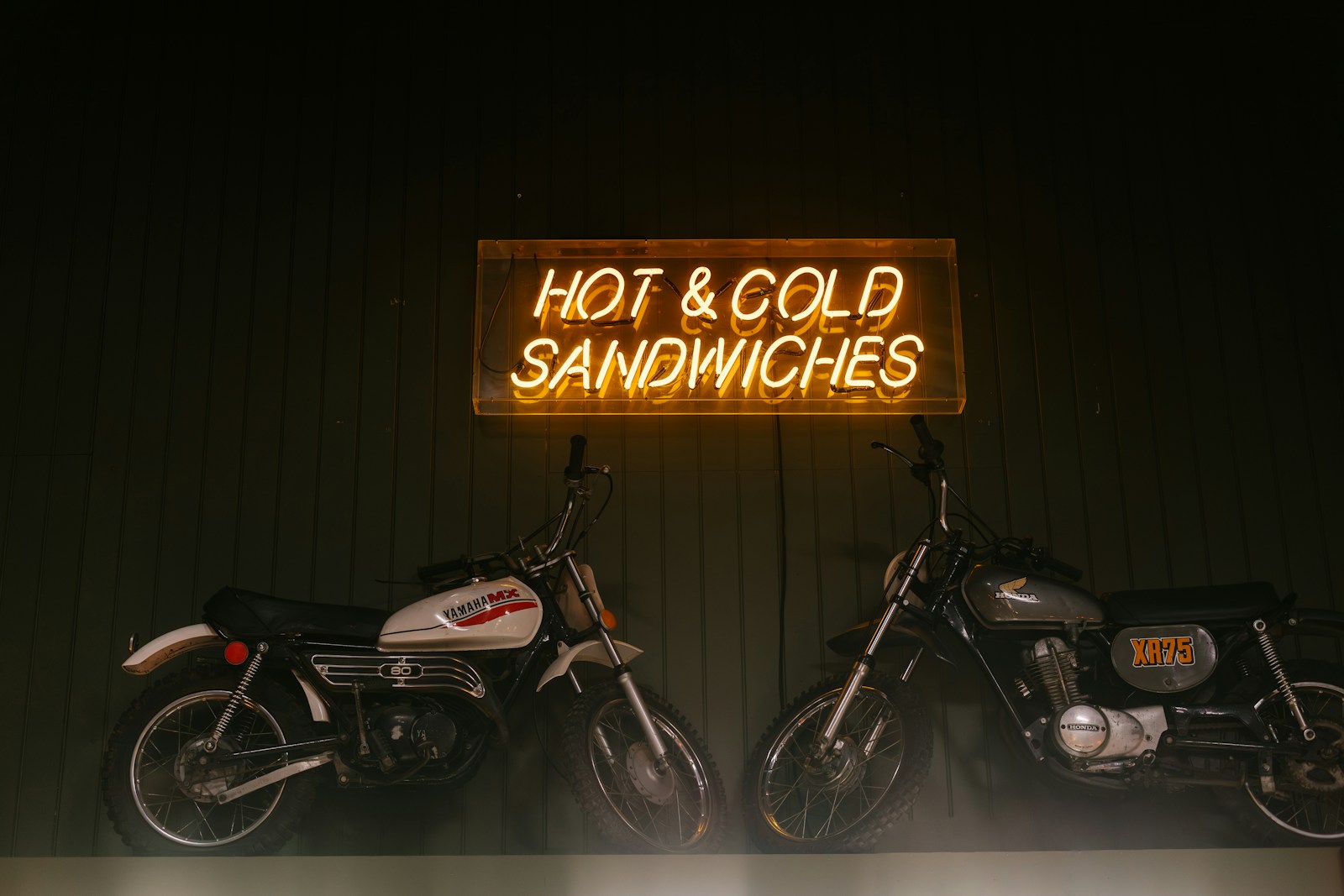 Neon sign advertises hot and cold sandwiches, with motorcycles.