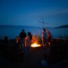 People gathered around a bonfire by the water at night.