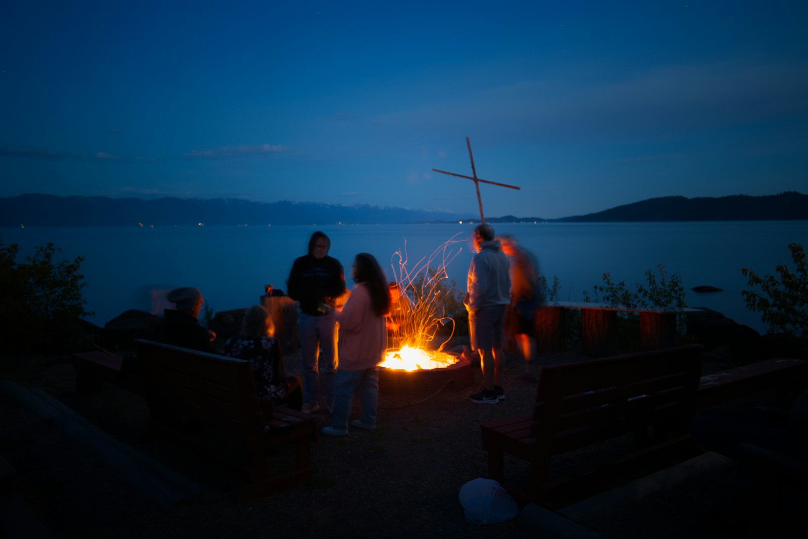 People gathered around a bonfire by the water at night.